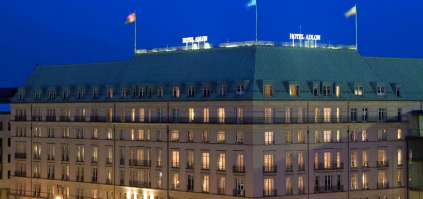 Grand hôtel éclairé au crépuscule avec drapeaux en toiture.
