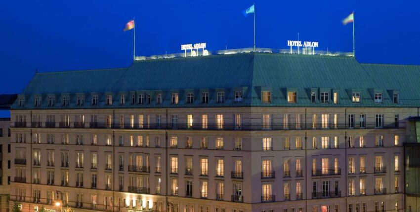 Grand hôtel éclairé au crépuscule avec drapeaux en toiture.