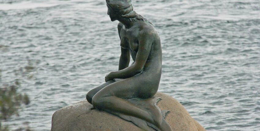 Une statue de sirène assise sur un rocher.