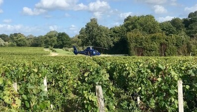location de jet privé : Hélicoptère sur vignobles verdoyants et ciel partiellement nuageux.