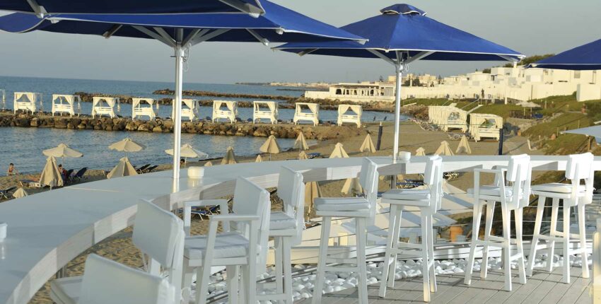Bar front de mer : chaises blanches, parasols bleus, plage