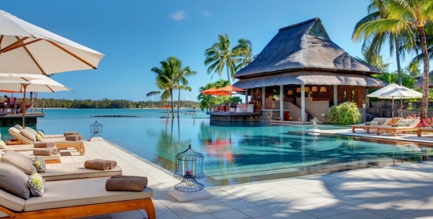 Resort tropical : piscine, transats, pavillon, palmiers.