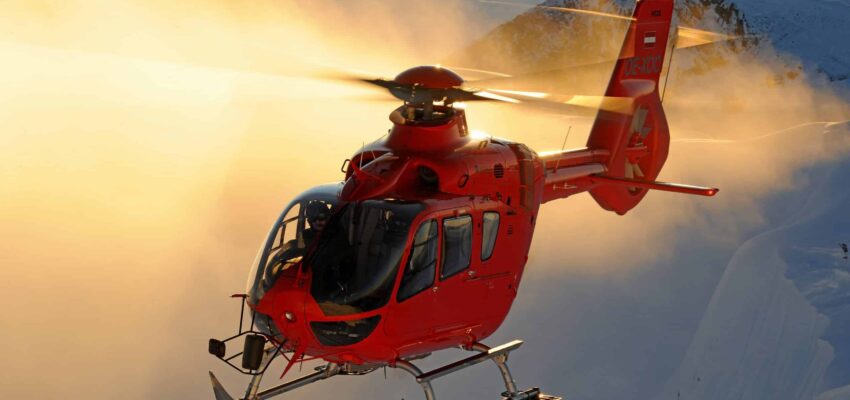 Hélicoptère rouge au coucher du soleil, montagnes en arrière-plan.