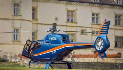 Hélicoptère bleu à rayures orange devant bâtiment.