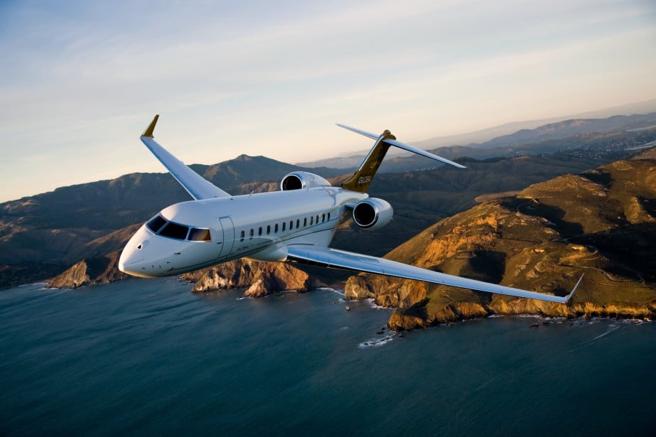 Le jet privé Bombardier Global 6000 en vol avec un couché de soleil, la mer et des montages