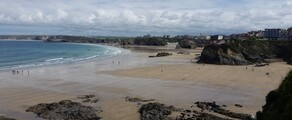 Plage Newquay, Cornouailles avec falaises rocheuses et bâtiments.