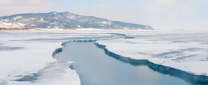 Glace craquelée sur un lac gelé avec des montagnes enneigées sous un ciel nuageux au loin, rappelant les paysages pittoresques près d'Irkutsk. - AEROAFFAIRES