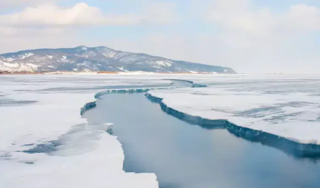 Glace craquelée sur un lac gelé avec des montagnes enneigées sous un ciel nuageux au loin, rappelant les paysages pittoresques près d'Irkutsk. - AEROAFFAIRES
