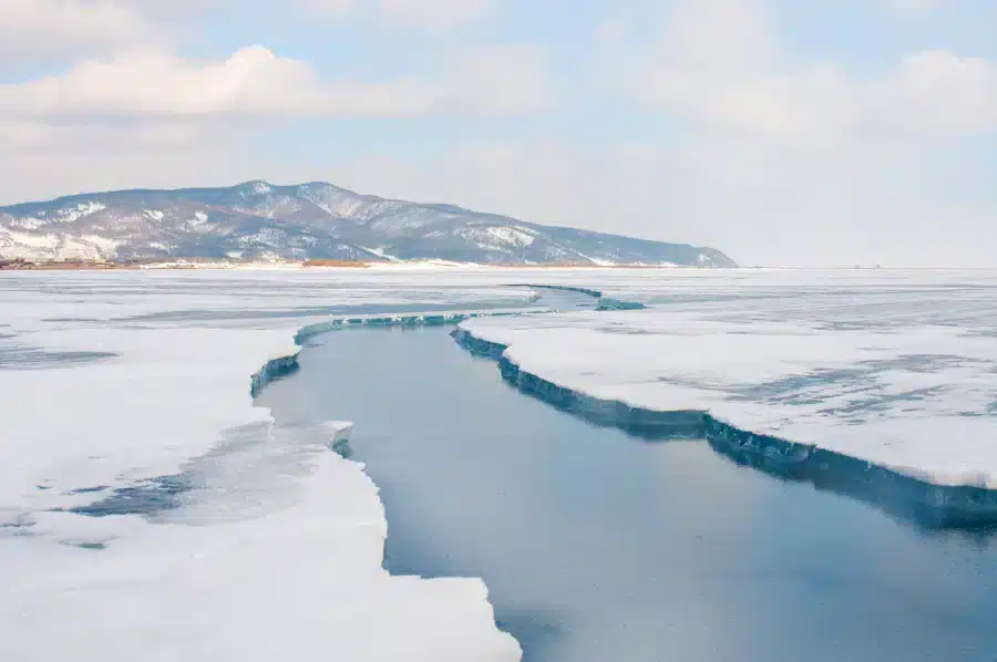 Glace craquelée sur un lac gelé avec des montagnes enneigées sous un ciel nuageux au loin, rappelant les paysages pittoresques près d'Irkutsk. - AEROAFFAIRES