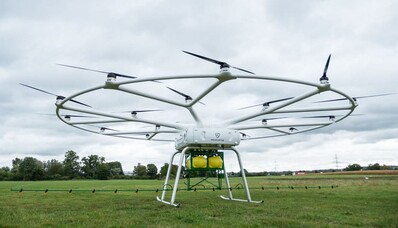 VOLODRONE survolant un champ herbeux sous ciel nuageux.